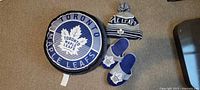 Top view of a round pillow with Toronto Maple Leafs logo, blue slippers with logo, and blue and white knit toque with pom-pom