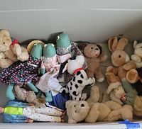 Photo of multiple stuffed animals including frogs, teddy bears, rabbits, a Dalmatian dog plush toy and more, some dressed in fabric clothing, arranged together.