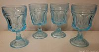 Four vintage baby blue tinted glass goblets side by side showing their overall shape and color.