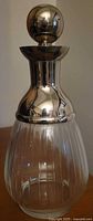Photo showing the full decanter, highlighting clear ribbed crystal body and shiny rounded silver-tone metal stopper top.