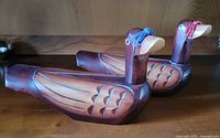 Two vintage hand carved wooden ducks side by side, highlighting the full profile and feather carvings with blue and pink tassels on bills