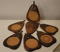 Seven pear shaped wooden coasters with cork centers displayed together on a flat surface.