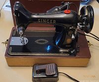 Front side view of the black vintage Singer sewing machine with gold accents, showing foot pedal and sewing area.