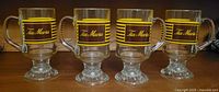 Front view of all four vintage Tia Maria clear glass footed mugs in a straight line.