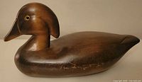 Front angled side view of wooden wood duck decoy, showing carved head and body with worn brown finish and inset painted eyes.