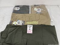 All four pairs of pants, two green two tan; two in plastic, two laid out
