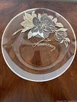 Top view of clear glass decorative plate showing silver floral design and '25th Anniversary' inscription.