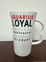 Front view of tall white ceramic mug featuring Aquarius zodiac traits in multi-colored text (red, black, gray).