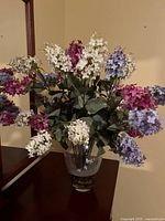 Front view of artificial hydrangea flower arrangement showing multiple colors in glass vase on dark surface near wall and mirror.