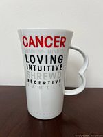 Front view of tall white ceramic mug showing 'CANCER' in red and descriptive words in black and gray text.