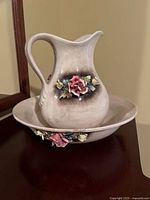 Ceramic pitcher and bowl set with 3D floral appliques set on wood surface, showing front and side profile of pitcher and bowl.