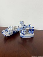 Blue and white Delft style porcelain windmill with kissing couple figurine next to decorative clog on wooden surface.