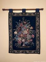 Full view of the woven floral tapestry wall hanging on the rod, showing the detailed floral design and border.