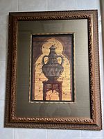 Full view of framed decorative print showing the ornate vase on pedestal with detailed frame and fabric mat.