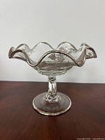 Side view of clear glass pedestal candy dish showing scalloped edge and silver overlay with floral patterns.