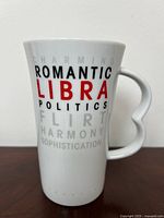 White ceramic mug with Libra zodiac sign text in black, red, gray on body, photographed front side show text clearly.