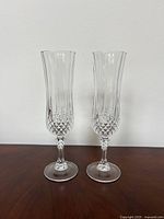 Two clear crystal champagne flutes standing side by side against a plain wall, showing full height and cut glass detailing.