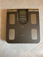 Top-down photo of the scale showing the full device including four metallic electrode pads and the Omron brand name on the surface.
