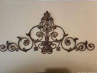 Full view of the ornate bronze metal wall art mounted on a wall, showing the symmetrical scroll and floral pattern.