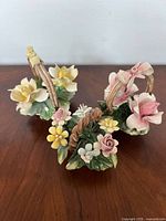 Photo showing three porcelain baskets with various pastel-colored flowers and green leaves on a wooden surface against a white wall.
