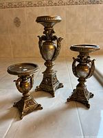 Set of three resin candle holders with faux bronze finish in vintage baroque style arranged on tile surface