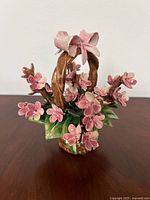 Front angle image showing ceramic floral arrangement with pink flowers, green leaves, and braided handle.