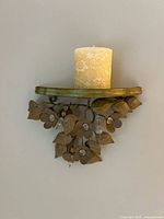 Front view of wall-mounted candle holder with lace-patterned pillar candle displayed on shelf with metal leaf and flower design.
