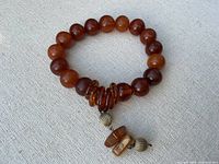 Full view of the bracelet showing round amber beads strung into a circle with a pendant section of flat amber rings and faux gold-tone baubles.