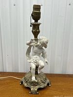 Full view of the antique brass and bisque cherub lamp showing the entire lamp including the brass base, cherub figure, and bulb socket with pull chain.