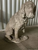 Side view of antique cement dog statue showing textured surface and missing parts on front leg and tail.
