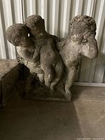 Front view of antique cement garden statuary showing three cupids in classical style with signs of wear and age.
