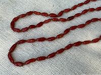 Close-up of the polished red coral beads showing texture, shape, and color variations on a neutral fabric background.