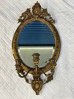 Front view of the antique oval gilt mirror with attached candle holders showing detailed frame and candle arms.