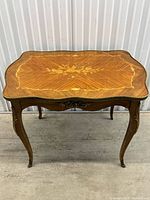 Front angled view of antique French coffee table with wood inlaid floral top and brass accents on legs and apron, showing wood grain and decorative details.