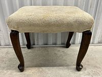 Front view of antique footstool with beige stained cushion and dark carved walnut legs.