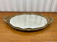 Front angled view of ornate gilt brass vanity tray with mirrored top showing detailed frame and feet