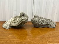 Front view of both cement bird statues side by side on wooden surface.