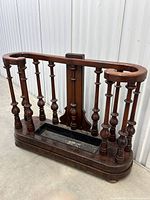 Front angle of antique walnut double umbrella/walking stick stand showing turned spindles and tray base with wear.