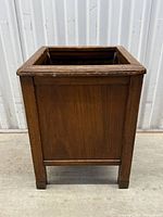 Front side of antique walnut waste paper basket showing solid wood panel and squared frame with wear marks.
