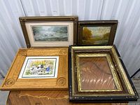 Group image showing four framed pieces including two prints, one oil painting, one empty frame, and portfolio case.