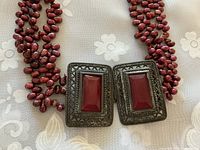 Close-up view of belt-buckle style metal closure with red glass inset on necklace