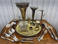 Overview of the lot showing silver-tone tray, vases, glass bowl, silver-plated flatware including tablespoons, salad forks, serving knife and fork, candle holders and tongs. Visible patina and wear on metal surfaces.