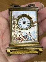 Clock held in hand showing front panel with cupids and clock face