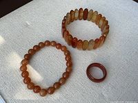 Top view of two agate bracelets and one agate ring displayed on light fabric showing colors and shapes clearly.
