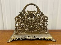 Front view of ornate gilt metal letter holder showing intricate filigree design and handle.