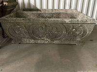Side view of one long vintage cement planter showing detailed raised scrollwork design and weathered surface