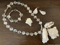 Full set of rock crystal necklace, bracelet and earrings laid out showing all pieces.