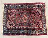 Full view of the small antique Persian rug laid flat to show entire design and shape.
