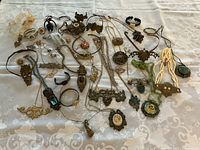 Full view of all jewelry pieces laid out on a patterned cloth background showing variety of necklaces, bracelets, rings, and brooches with steampunk and vintage design elements.