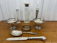 Overview of all items in lot displayed on a wooden surface: vase, two pedestal bowls, serving spoon, knife, and silver ring.
